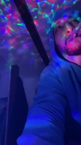Person in hoodie observed in colorful lit spaces, Bischheim