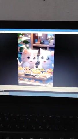 A laptop is shown displaying a video of two cartoon kittens, one white and one orange-and-white, sitting behind a table laden with various food items. The laptop keyboard is visible in the lower portion of the frame, and parts of the desktop computer interface are visible above the video. A "CapCut" logo is visible in the top left of the video, suggesting it may be sourced from the CapCut application.  Sounds of a kitten are audible. The surrounding environment is basic, with a plain wall behind the laptop.