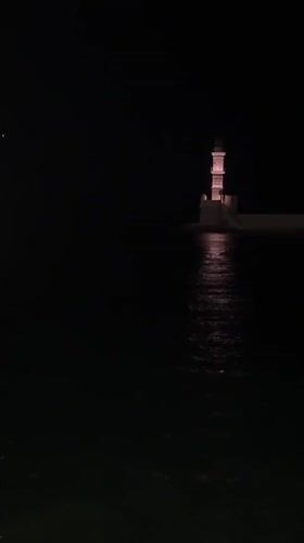 Chania harbor at night — lighthouse, boats, and old town streets