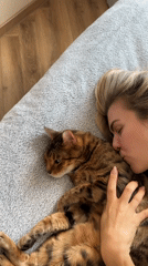 Woman cuddles with Bengal cat on bed during afternoon rest