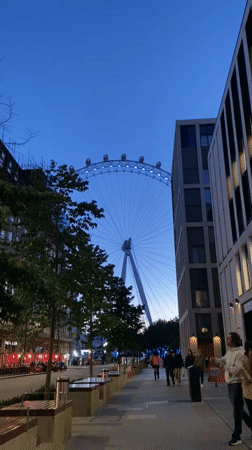 London Eye glows blue at dusk, witnessed from street level