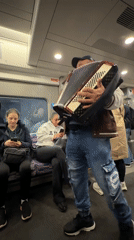 Street musician performs accordion on London train