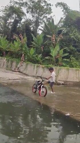 Boy walks bicycle through shallow water in Saweuk, Indonesia