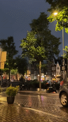 Rainy Amsterdam street at night, lights reflecting on wet pavement.