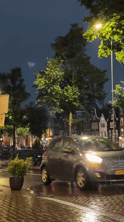 Rainy Amsterdam street at night, lights reflecting on wet pavement.