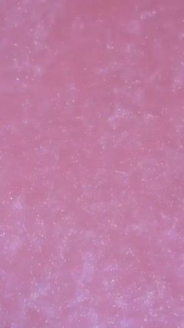 The video is a close-up, static shot of a pink surface with shimmering particles. The particles appear to be small and reflective, scattered across the surface. The lighting creates a subtle glow and highlights the texture of the surface. There are no discernible objects, people, or actions taking place. The background is uniformly pink.