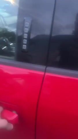 The video shows the interior of a red Ford F-150 truck. The camera is positioned just inside the open driver's side door, looking into the cabin. We see the steering wheel, dashboard, center console with gear shifter, and the driver's seat. There is a piece of paper on the floor in front of the driver's seat, with text visible. Other vehicles are partially visible through the windows of the truck, suggesting it is in a lot. The lighting is dim, possibly indicating evening or an overcast day.
