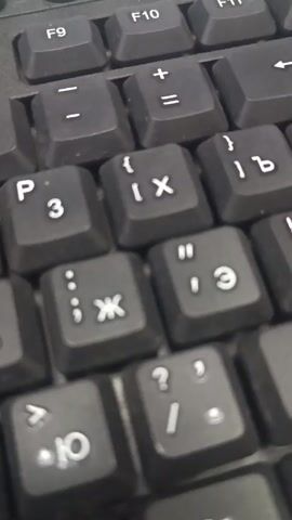The video shows a close-up view of a black computer keyboard. The focus is on the keys with letters in Cyrillic alphabet alongside Latin letters and symbols. The video zooms in slightly, emphasizing the detail on the keys. The keyboard appears to be dusty.
