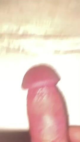 The media file is a close-up, static shot of a person's hand holding a penis. The background is a wooden surface with a light-colored grain. There are no discernible location cues other than the provided context of "Нарынка, Russia." The lighting appears to be artificial and is casting a shadow from the penis onto the wooden surface. The image is a still from a video, as indicated by the timestamp at the beginning of the file. No text is visible in the media. The activity depicted is the presentation of a human body part.