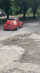 Red Volkswagen Beetle drives on wet road in Razgrad