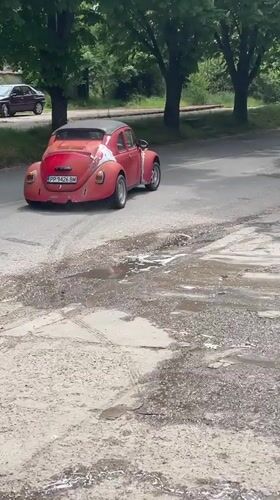 Red Volkswagen Beetle drives on wet road in Razgrad