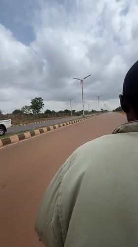 Motorcyclist in green jacket travels paved road in Nigeria