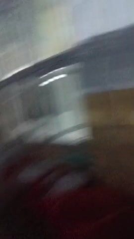The video appears to be filmed from a low angle, possibly from a phone being carried by someone walking. The first few seconds show a blurry, bright interior with what looks like windows or openings in a ceiling. The camera then pans downwards, showing a wooden surface and then transitions to a darker hallway. A person, silhouetted and facing away from the camera, is seen walking down the hallway. The hallway has yellow and black striped barriers on the floor and doorways leading off it. The overall impression is of someone moving through an institutional or utilitarian building, possibly at night or in a dimly lit area.