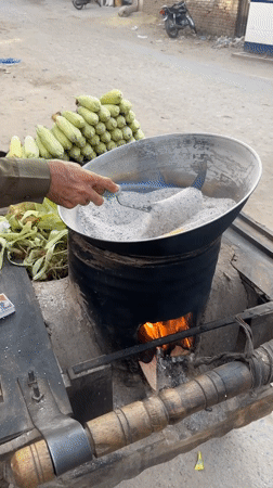 Street vendor roasts corn using hot sand method in Multan