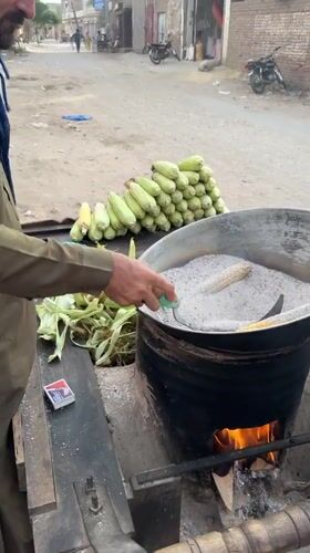 Street vendor roasts corn using hot sand method in Multan