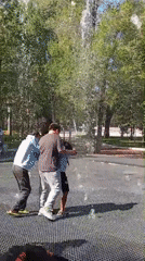Kids play in a ground-level fountain on a sunny Kostanay day