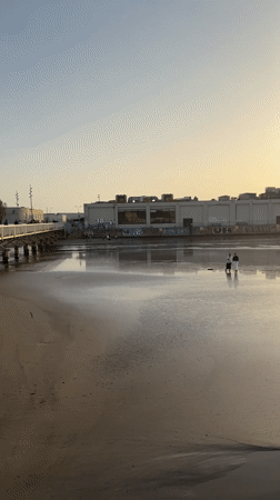 Two people walk along sunlit Tel Aviv beach