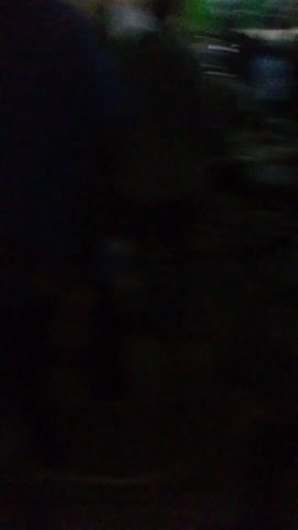 The video begins in a dark setting, then rapidly transitions to a brighter indoor scene. A large group of people are seated in rows, facing a screen, and a person walks past the camera. There is text visible on the floor. The overall lighting is poor.