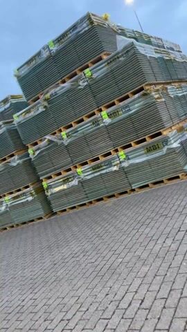 The video shows a brief tour of what appears to be a loading dock or warehousing area. At the start, there are large stacks of what look like palletized materials, possibly building supplies, covered in plastic wrap, set on wooden pallets. The video moves to show the paved area, street lighting, and then the exterior of a building with a loading dock area marked with yellow and black safety barriers. The camera then enters what seems to be a loading bay with large yellow doors and an interior shot shows a space with pallets and other materials. The entire video is brief and seems to be a quick tour of the area.