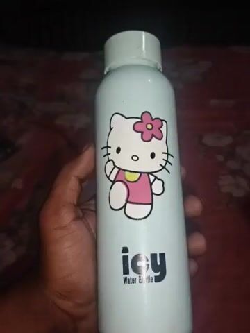 A person's hand holds a light blue water bottle with a Hello Kitty design. The bottle also has the word "icy" and "Water Bottle" printed on it in black. The background is a blurry, reddish, patterned surface. The video consists of a single, static shot.