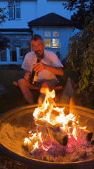Man enjoys evening wine by backyard fire pit in Stotfold