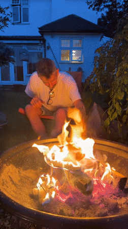 Man enjoys evening wine by backyard fire pit in Stotfold