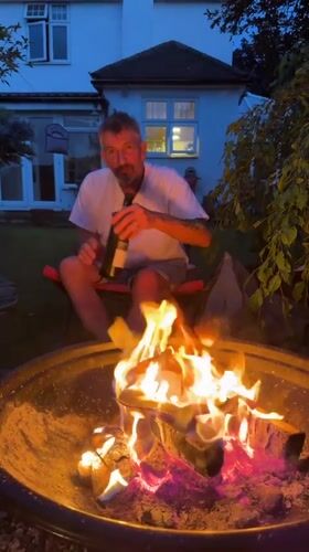 Man enjoys evening wine by backyard fire pit in Stotfold