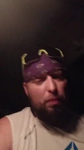 Here's a description of the video. 

The video features a close-up shot of a man from the chest up. He has a beard and wears a white shirt with a blue and green logo, a purple paisley bandana, and sunglasses with yellow frames pushed up on his forehead. He appears to be inside a vehicle, likely the driver's seat, judging by the lighting and the interior of the car visible in the background. He is talking directly to the camera, seemingly delivering a message.