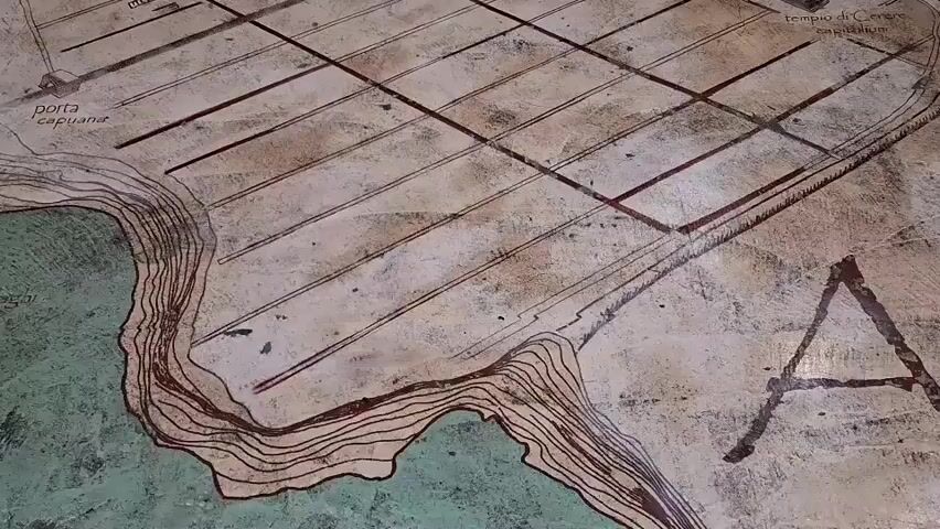 The video shows a close-up view of an ancient map, likely etched or painted onto a stone surface. The map depicts a city with a grid-like street layout, suggesting Roman urban planning. Prominent features include structures resembling an amphitheater and a theater, along with labeled areas such as "Porta Capuana," "Via Latina," and "Porta Romana." Contour lines indicate varying terrain, and a body of water, possibly a river or coastline, is visible along one edge of the map. The map itself appears weathered and aged, with some areas showing signs of wear and tear. The lighting is somewhat dim, with the light source creating shadows that highlight the texture of the map. The camera slowly pans across different sections of the map, allowing viewers to observe the intricate details of the ancient cartography.