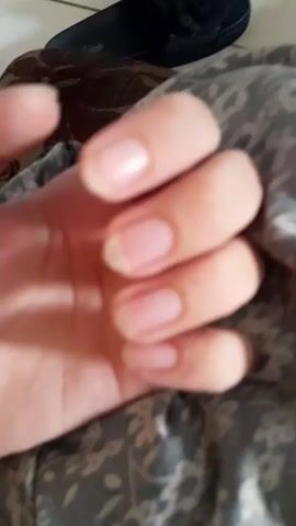 The video shows a close-up of a person's hand with natural, unpolished fingernails. The hand is positioned over a patterned fabric. In the background, a dark slipper with a decorative bow and a ring is visible on a tiled surface. The hand moves slightly throughout the video, with some frames showing the fingers in a slightly curled position and others more spread out.