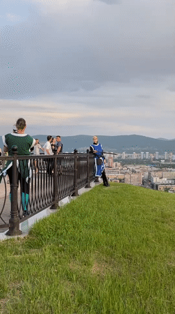 Person checks phone while leaning over railing at Krasnoyarsk overlook