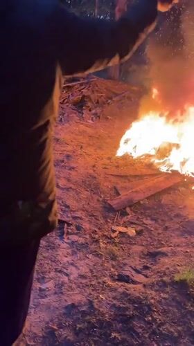 Person tends bonfire near wooden structure in Russian village