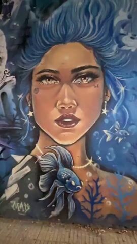 The video shows a close-up of a mural. The mural depicts a woman with blue hair, a fish, an octopus, a dragon, and purple graffiti-style lettering. The octopus is pink and has yellow eyes.