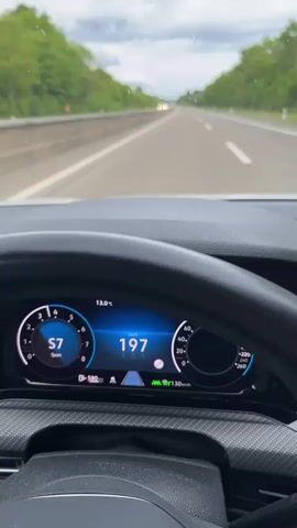 The view from inside a vehicle shows the digital dashboard and the open road ahead. The speedometer climbs from 197 to 201 kilometers per hour, in sport mode. The vehicle is on a highway with trees visible on both sides. The sky is overcast. There is other traffic visible in the distance. The dashboard also shows the time as 10:19 and the temperature as 13.3 degrees Celsius.