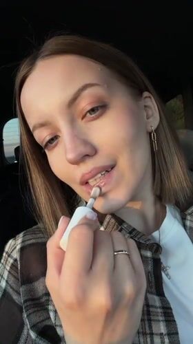 Woman applies lip gloss in car in Rogachovo