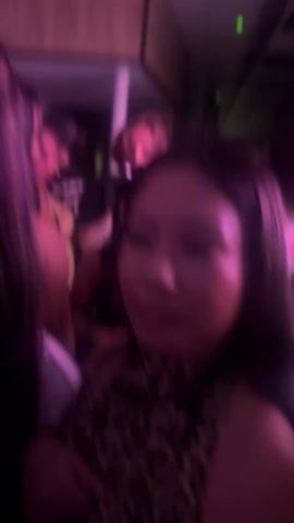A close-up, slightly shaky video shows a person wearing a leopard-print top. Their arm, adorned with a watch and a tattoo, is visible. The lighting is dim and has a pink hue. The focus appears soft, and the overall scene is somewhat blurry. The person is seated, but there is no clear action or interaction.