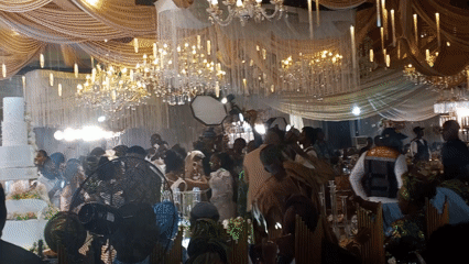 Wedding reception crowd gathers in decorated venue with cake