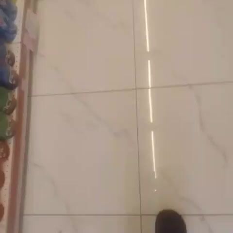 The video shows the shelves of a supermarket filled with various types of shampoos and body washes. The camera moves vertically and diagonally, showing different shelves containing bottles of various colors like pink, purple, yellow, and blue. The bottles are arranged on the shelves in rows, with several units of each color. The video ends by showing someone's feet as they stand in front of the shelves. The floor is composed of white marble-like tiles with dark veins. The overall lighting is bright, suggesting an indoor supermarket setting.