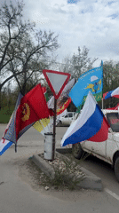 Multiple flags displayed on roadside yield sign in Volgograd