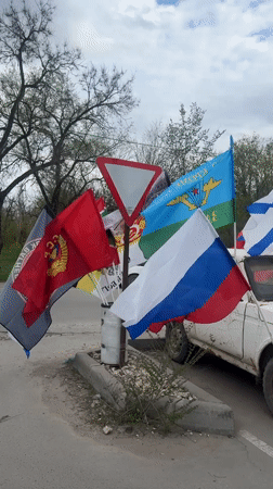 Multiple flags displayed on roadside yield sign in Volgograd