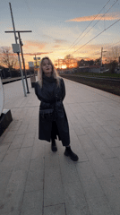 Woman dances, waits on train platform during sunset hours