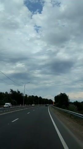The video shows a highway with a cloudy sky. There are trees on either side of the road, and some cars are driving on the highway. There are also streetlights along the side of the road and a speed limit sign of 60.