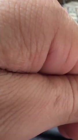 A close-up macro shot of human skin, showing the creases and texture of fingers or knuckles. The skin appears to be light-skinned with visible lines and pores. The focus is extremely tight on the skin, with the background softly blurred, suggesting a shallow depth of field. Towards the end of the clip, the camera pulls back slightly, revealing more of a hand and the surrounding environment, which includes what appears to be furniture and carpet. The lighting is soft and diffused.