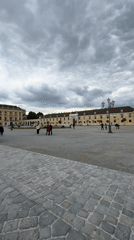 Tourists visit Schönbrunn Palace courtyard under cloudy Vienna skies