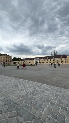 Tourists visit Schönbrunn Palace courtyard under cloudy Vienna skies