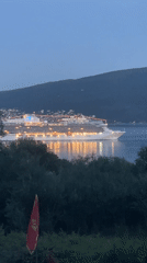 Illuminated cruise ship anchors at dusk in Baošići bay