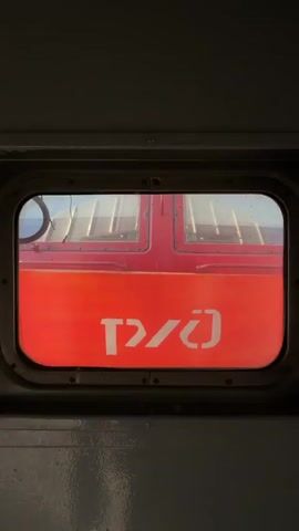 The view from a train window shows a bright red locomotive. The words “RZD” are visible in white Cyrillic letters on the side of the locomotive. A window frame surrounds the image. The view is still and the video is brief.