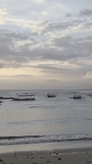 Outrigger boats rest on calm Bali coastal waters at golden hour.