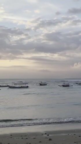Outrigger boats rest on calm Bali coastal waters at golden hour.