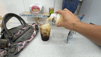 Person adds cream to iced coffee at Seoul convenience store